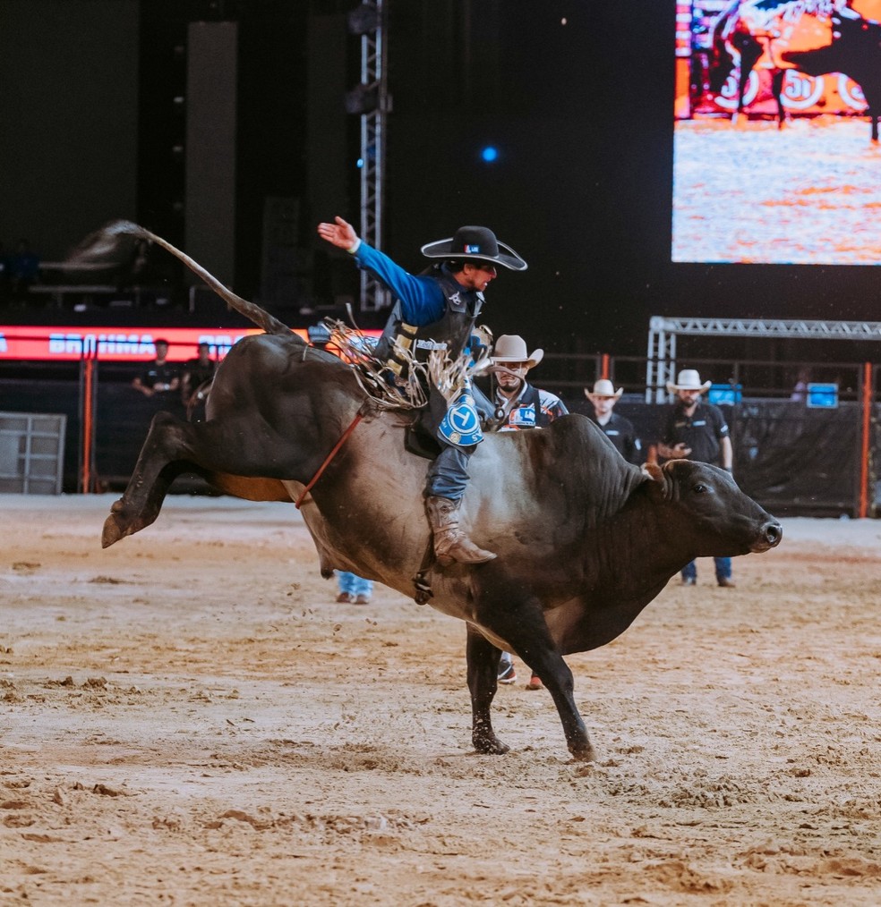 Imagem de um rodeio regional, com participantes montando em touros em um ambiente festivo e animado.