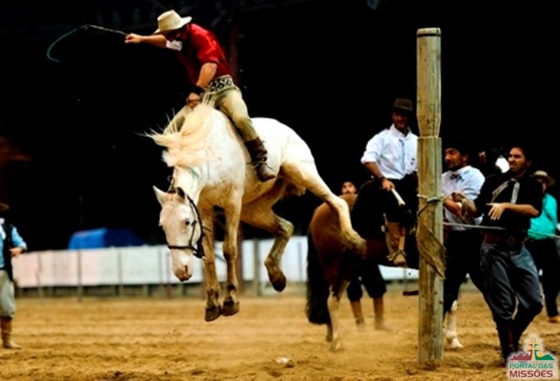 Participantes se divertindo em um rodeio regional, vestindo roupas típicas e montando em touros.