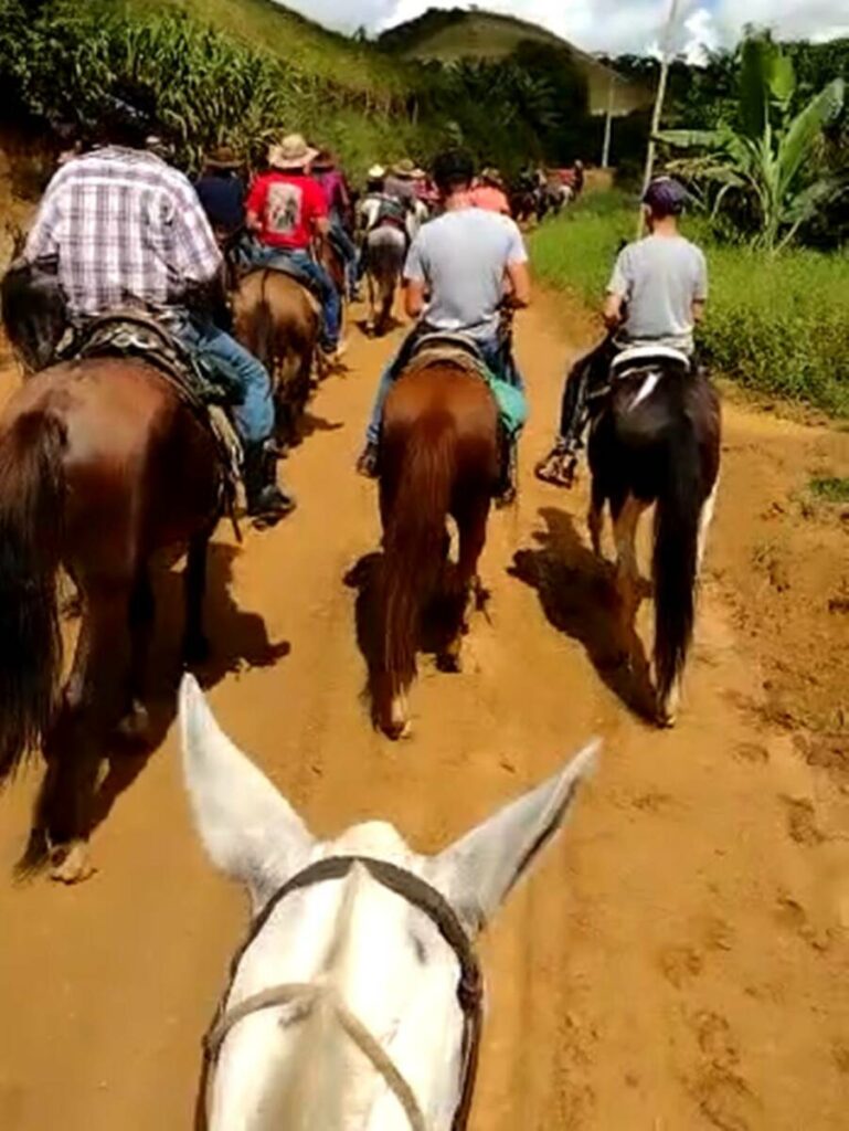 Cavalgada no interior do Brasil, mostrando cavaleiros e amazonas em um campo verdejante sob um céu azul.