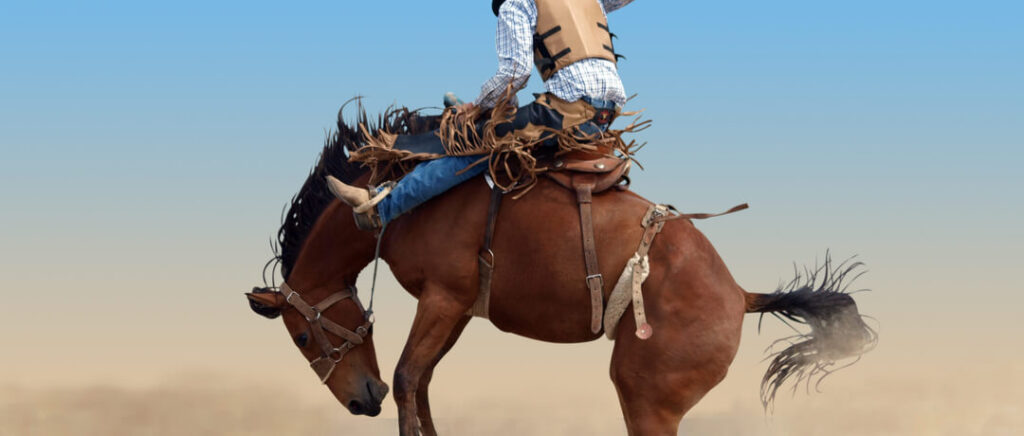 Montaria em cavalos em um evento de rodeio, com um cowboy em cima de um cavalo em ação.