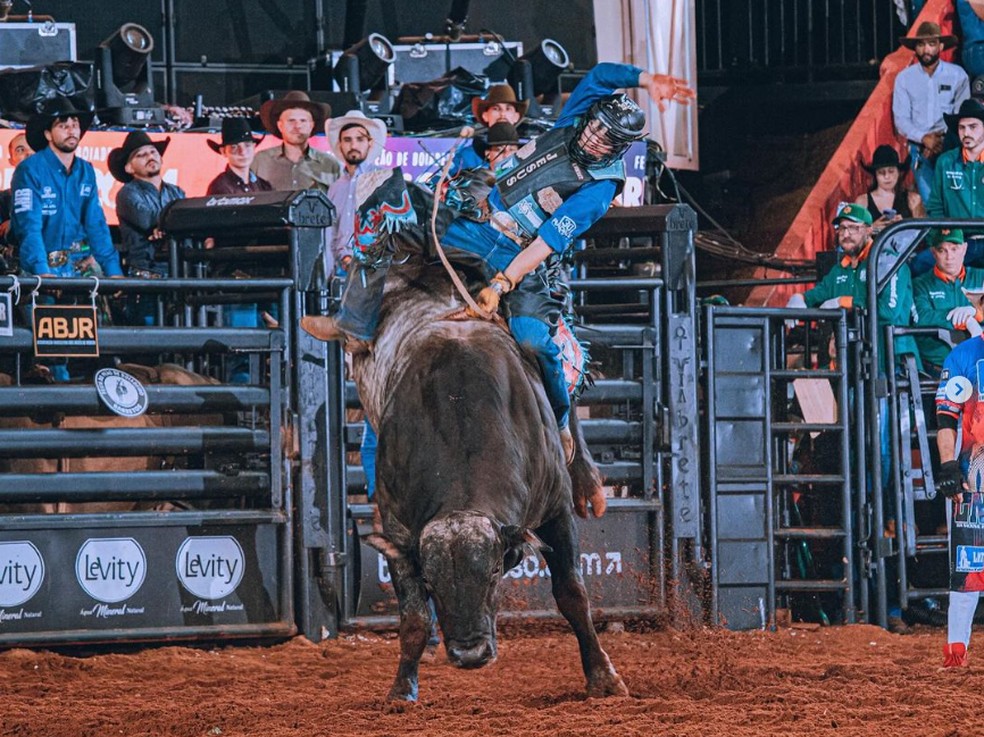 Um cowboy montando um touro durante uma competição de rodeio em um ambiente country.