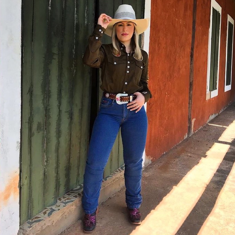 Um grupo de pessoas vestindo roupas típicas country, com chapéus de cowboy, botas e camisas xadrez, em um cenário rural.