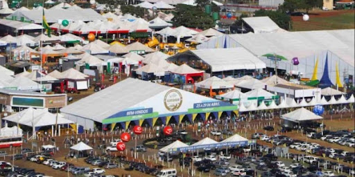 Visão panorâmica de uma feira agropecuária no Brasil, com estandes de diferentes tipos de produtos rurais e visitantes interagindo.