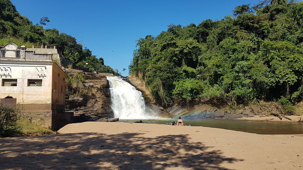 Uma paisagem rural do interior do Rio de Janeiro, com vacas pastando, montanhas ao fundo e um céu azul limpo, ideal para turismo rural e ecoturismo.