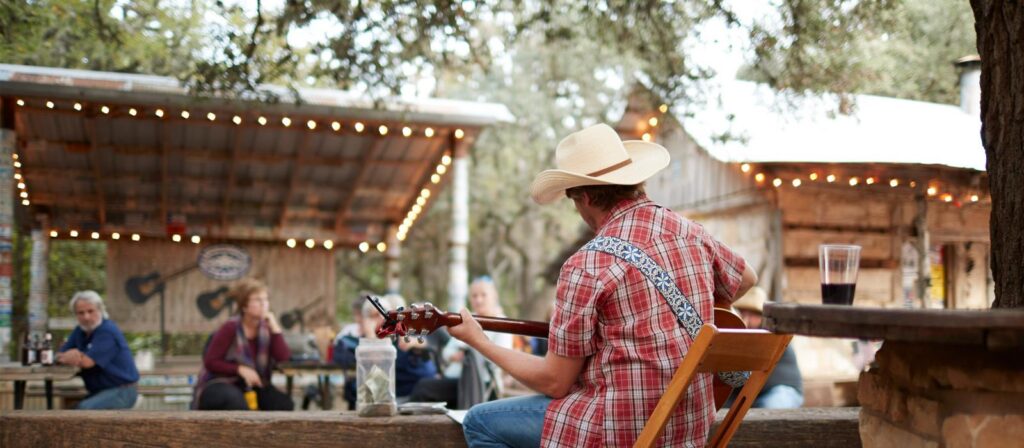 Um cowboy tocando violão sob um céu azul em uma paisagem rural americana