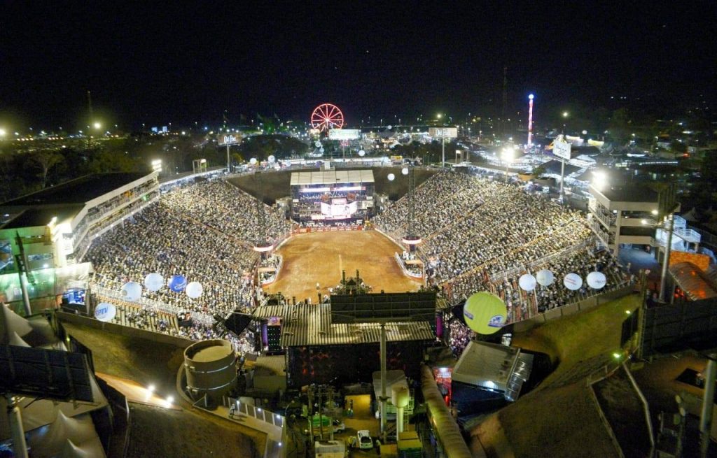 Festa do Peão de Barretos, com peões a competindo e aplaudindo, rodeio em um ambiente festivo.