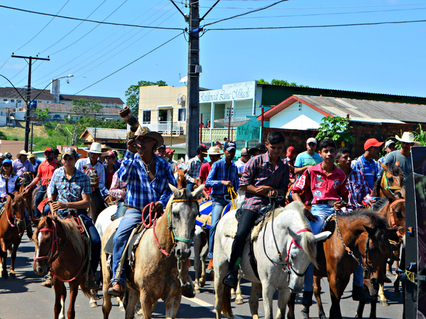 Cavaleiros e cavaleiras participando de uma cavalgada em homenagem ao campo, com um ambiente rural ao fundo.