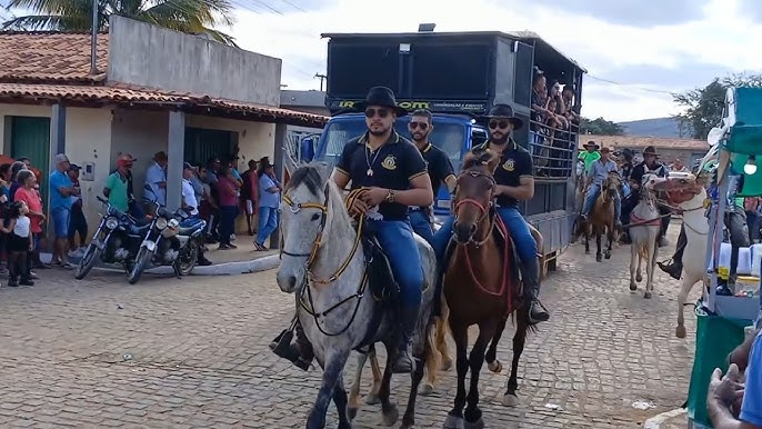 Cavalgada tradicional no interior, com cavaleiros e cavalos em um lindo campo verdejante.
