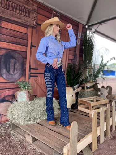 Mulher vestindo roupas country femininas, com chapéu e botas em um ambiente rural.
