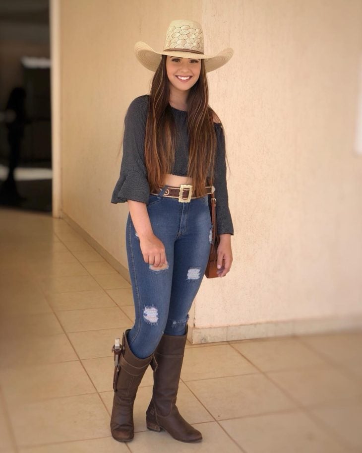 Mulher vestindo uma roupa country com estilo, destacando acessórios típicos como chapéu e botas.