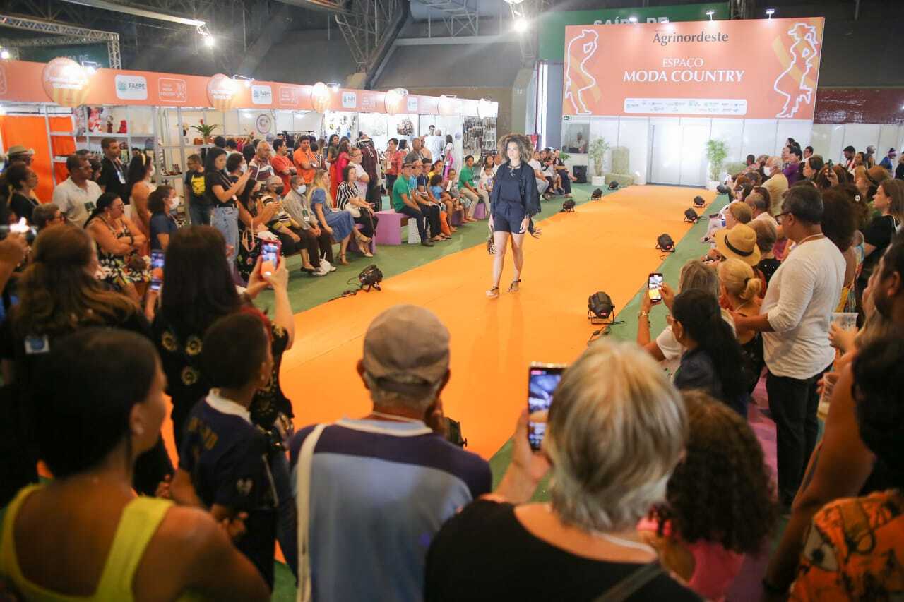 Desfile de moda country com modelos vestindo trajes típicos e acessórios tradicionais.