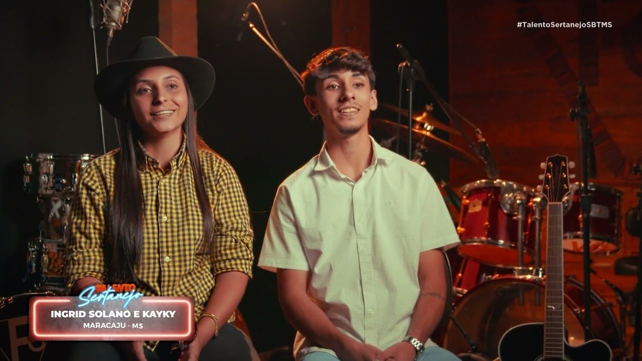 Artista sertanejo se apresentando em um palco iluminado, com o público aplaudindo.