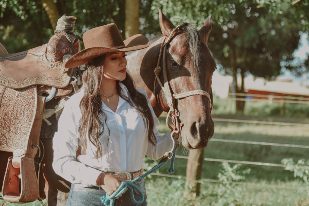 Competidor de rodeio se preparando para uma competição, vestido com trajes típicos country, enquanto cuida do seu animal.