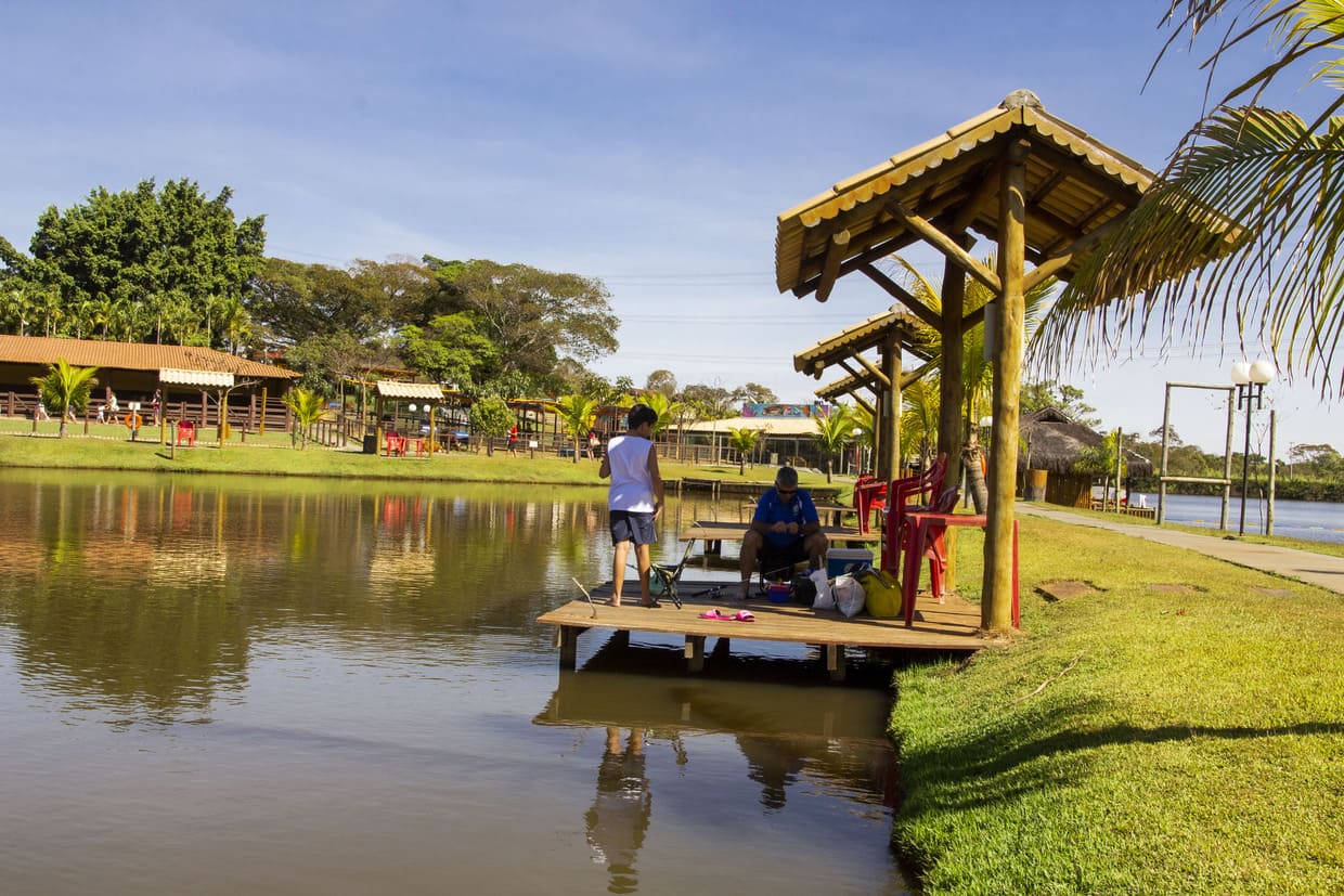 Um pescador relaxando à beira de um lago em Goiás, cercado por natureza exuberante.