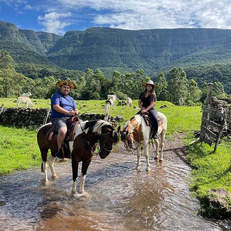 Cavalgada ao amanhecer com cavaleiros em um cenário rural, rodeado por montanhas e céu colorido.