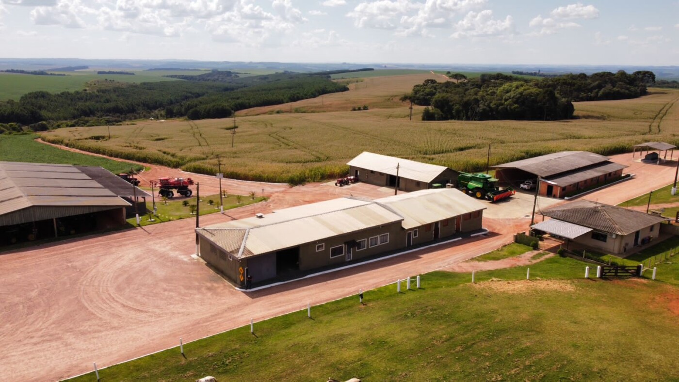 Uma vista panorâmica de uma fazenda com pastagens verdes e rebanhos de gado sob um céu azul.