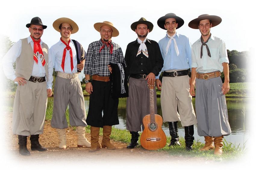 Homem vestindo trajes típicos de gaúcho no Rio Grande do Sul, com chimarrão e um cavalo ao fundo.