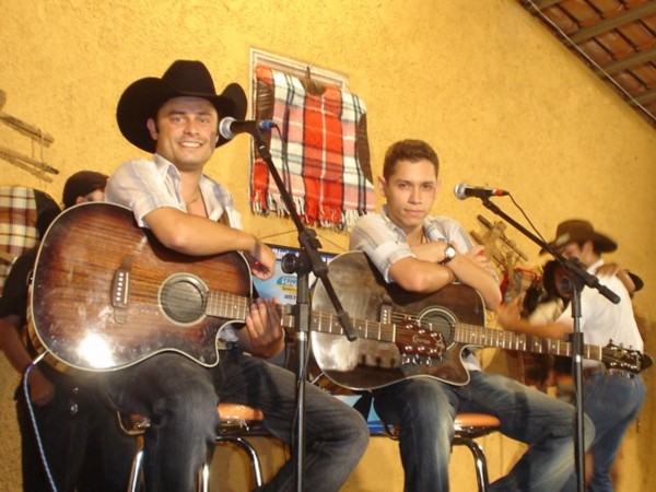 Artista sertanejo tocando violão em um cenário rural