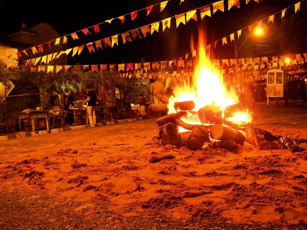 Festas Juninas no campo com bandeirinhas coloridas e pessoas dançando ao som de sanfona.