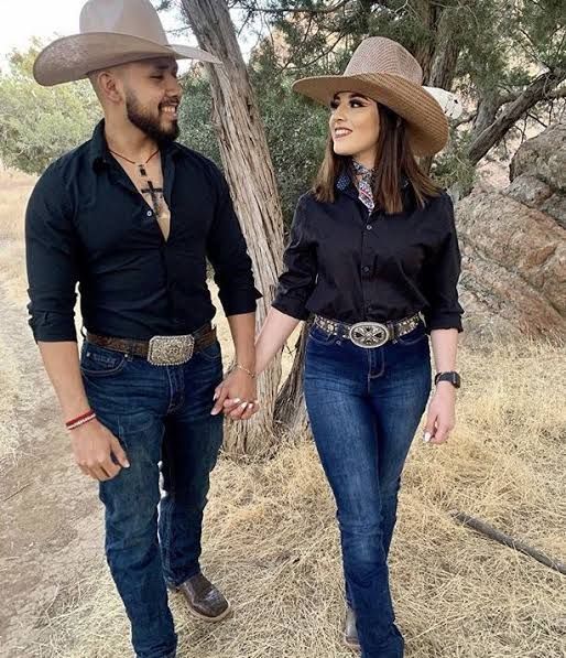 Casal vestido com estilos country, ele em uma camisa xadrez e ela em um vestido floral, ambos com acessórios de cowboy.