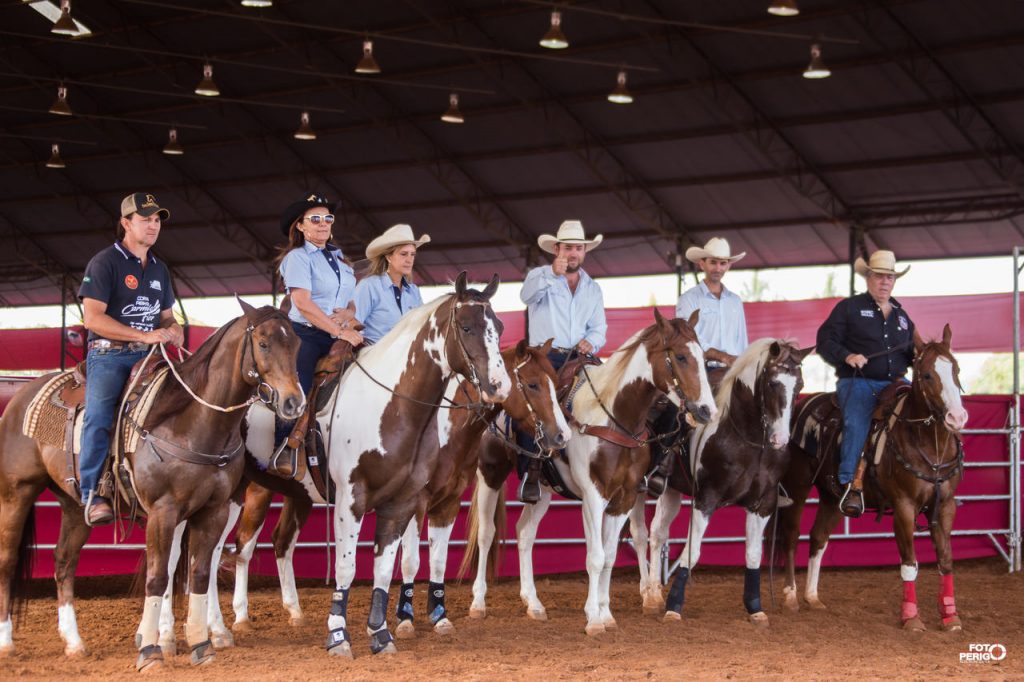 Cavaleiro preparando seu cavalo para competição equestre, com acessórios e equipamentos adequados em um ambiente de fazenda country.