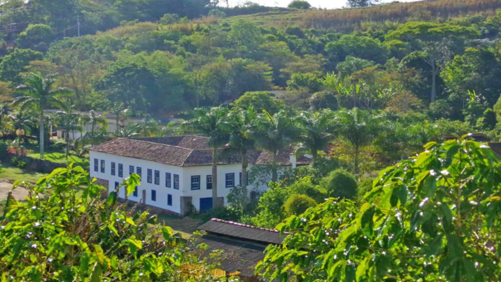 Cenário rural brasileiro com campos verdes, uma fazenda típica e céu azul.