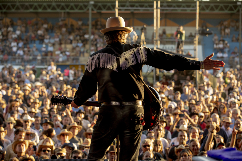 Público animado em um festival de música country, com bandas tocando e pessoas dançando.