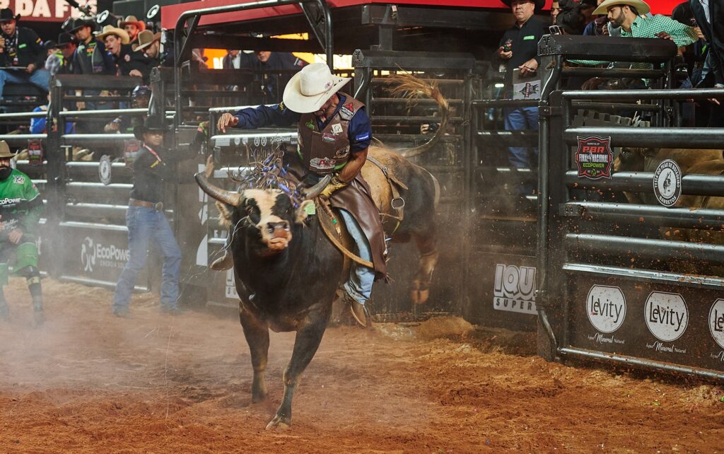 Montaria em touros durante a Festa do Peão de Barretos, com cowboys em ação e público animado ao fundo.