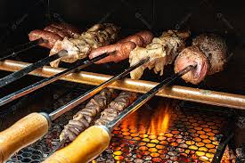 Churrasco sendo preparado na churrasqueira com carvão e fogo quente. Salsicha, carne e frango no espeto [download] - Designi